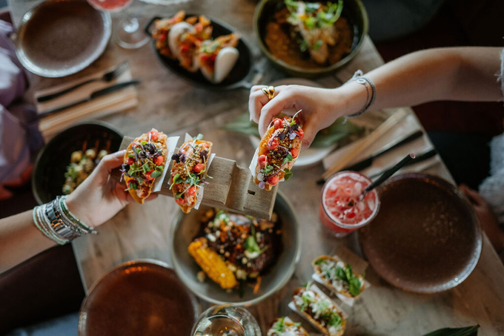 people holding tacos over restaurant table