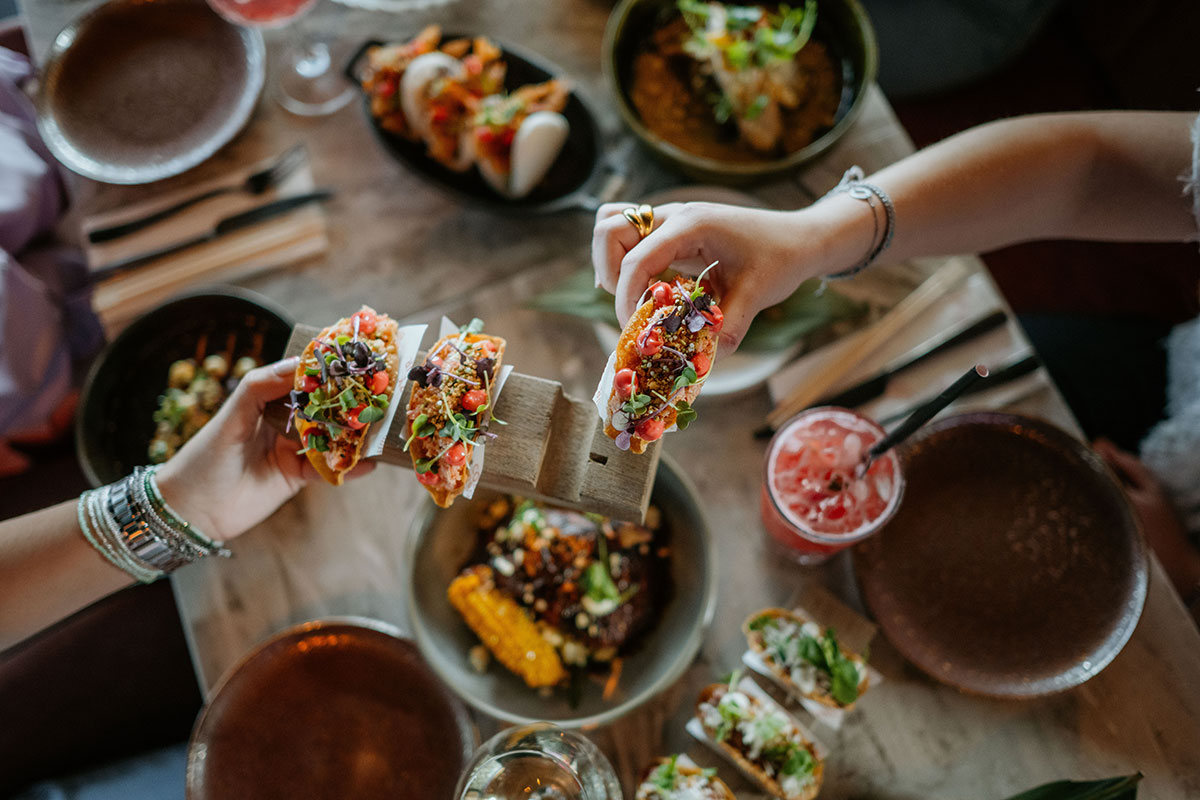 people holding tacos over restaurant table